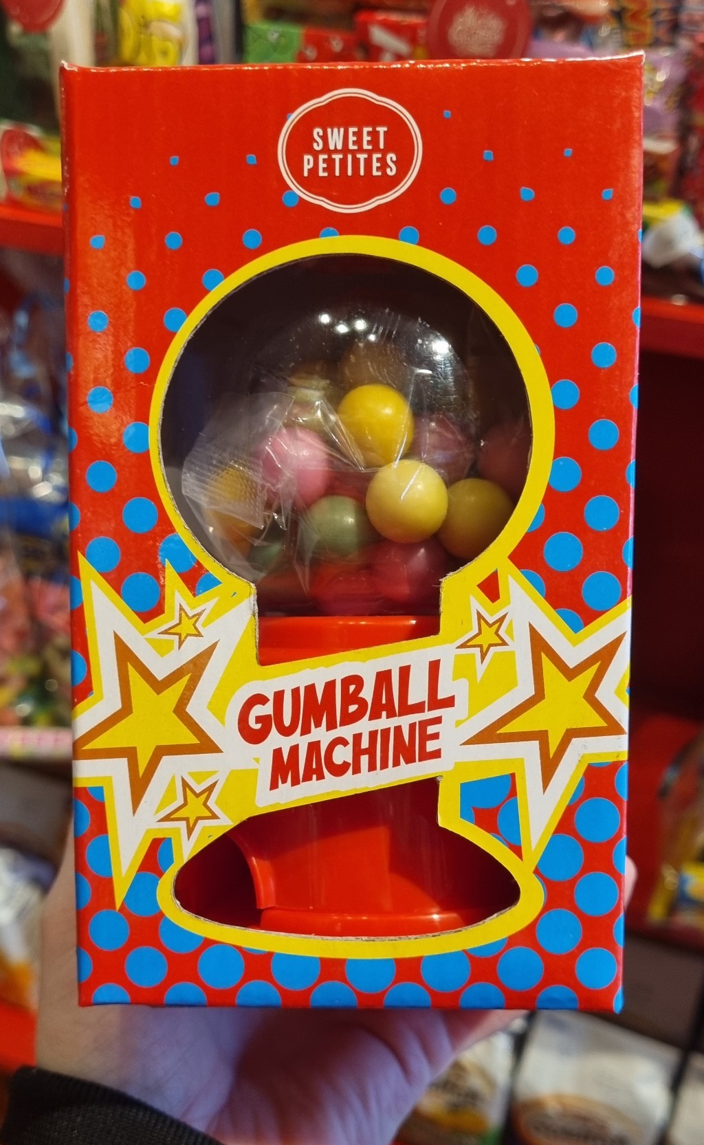 A mini gumball machine with colorful gumballs inside, packaged in a red box with graphics and a clear display window.