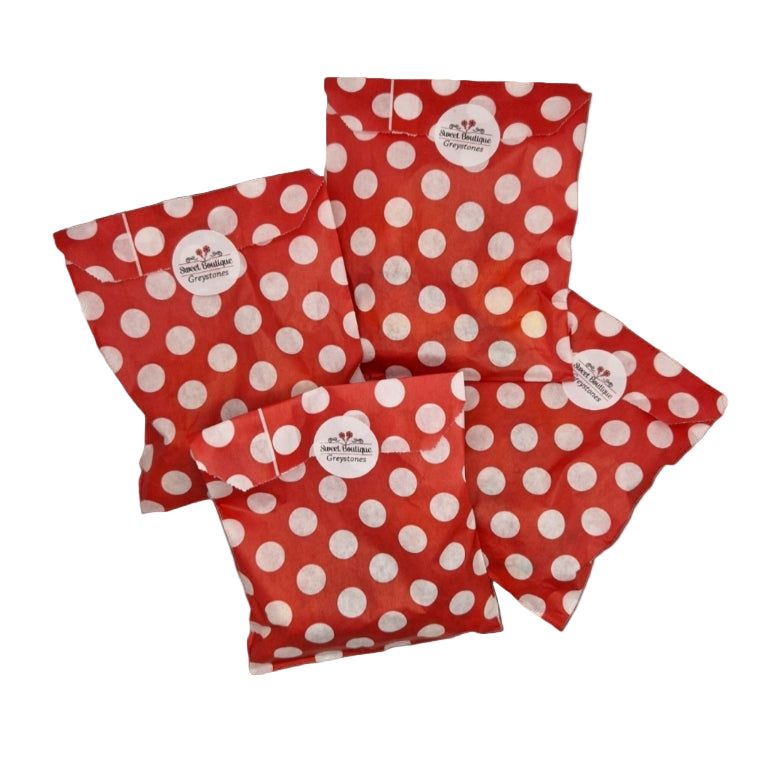 A collection of red paper party bags with white polka dots, filled with candy, on a white background.