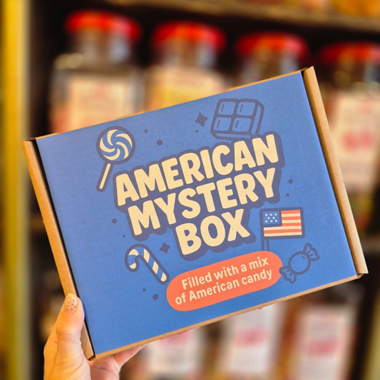 American Mystery Box packaging with text and graphics, held in front of blurred candy jars.
