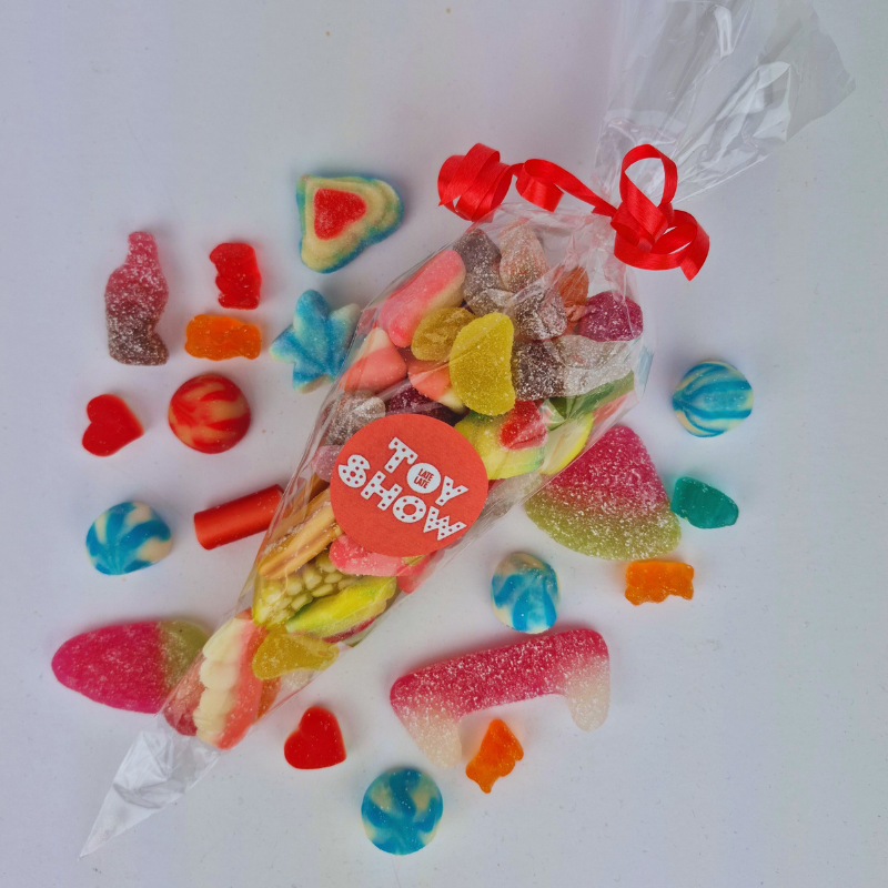 Colorful gummy candies spilling out of a clear bag with red handles on a white background.