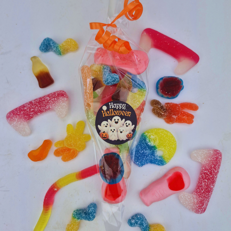 A clear plastic bag filled with assorted Halloween-themed gummy candies, tied with an orange ribbon and labeled 'Happy Halloween,' surrounded by loose gummy candies on a white background.