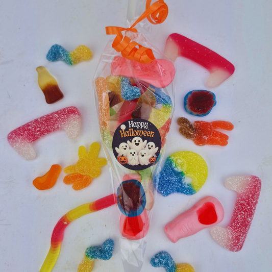 A clear plastic bag filled with assorted Halloween-themed gummy candies, tied with an orange ribbon and labeled 'Happy Halloween,' surrounded by loose gummy candies on a white background.